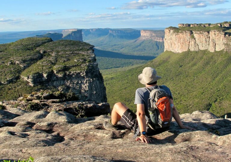 A hiker relaxes on a cliff in Chapada Diamantina, Brazil, overlooking stunning rock formations and lush greenery.