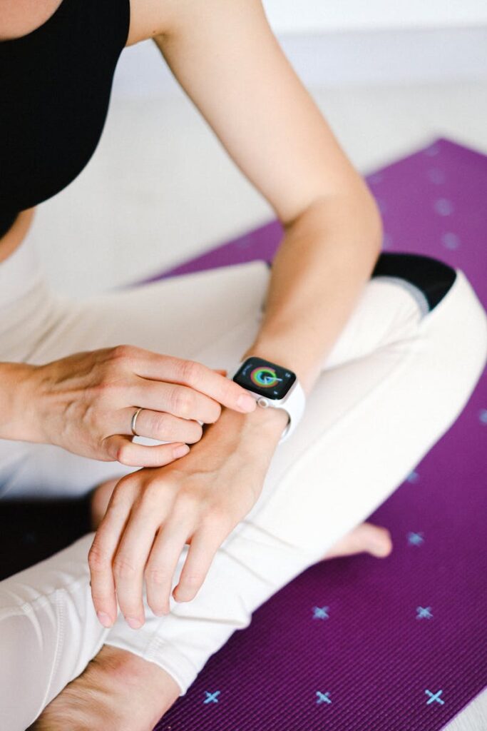 Close-up of woman adjusting smartwatch while sitting on a yoga mat, focusing on fitness and technology.