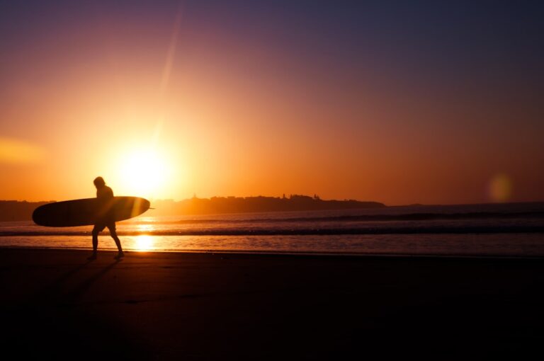 Silhueta de um homem segurando uma prancha de surfe perto da costa durante o pôr do sol.